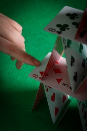 Photo of Woman destroying house of playing cards on green background, closeup