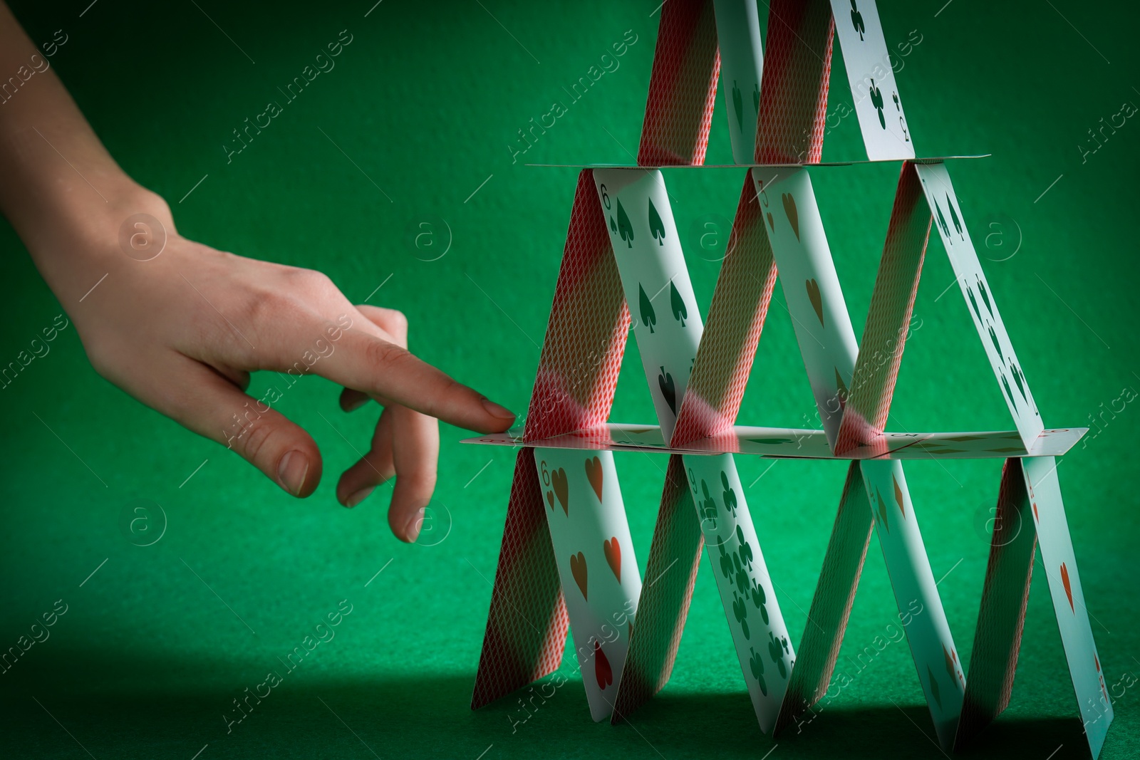 Photo of Woman destroying house of playing cards on green background, closeup