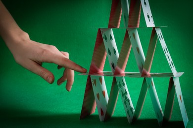 Photo of Woman destroying house of playing cards on green background, closeup