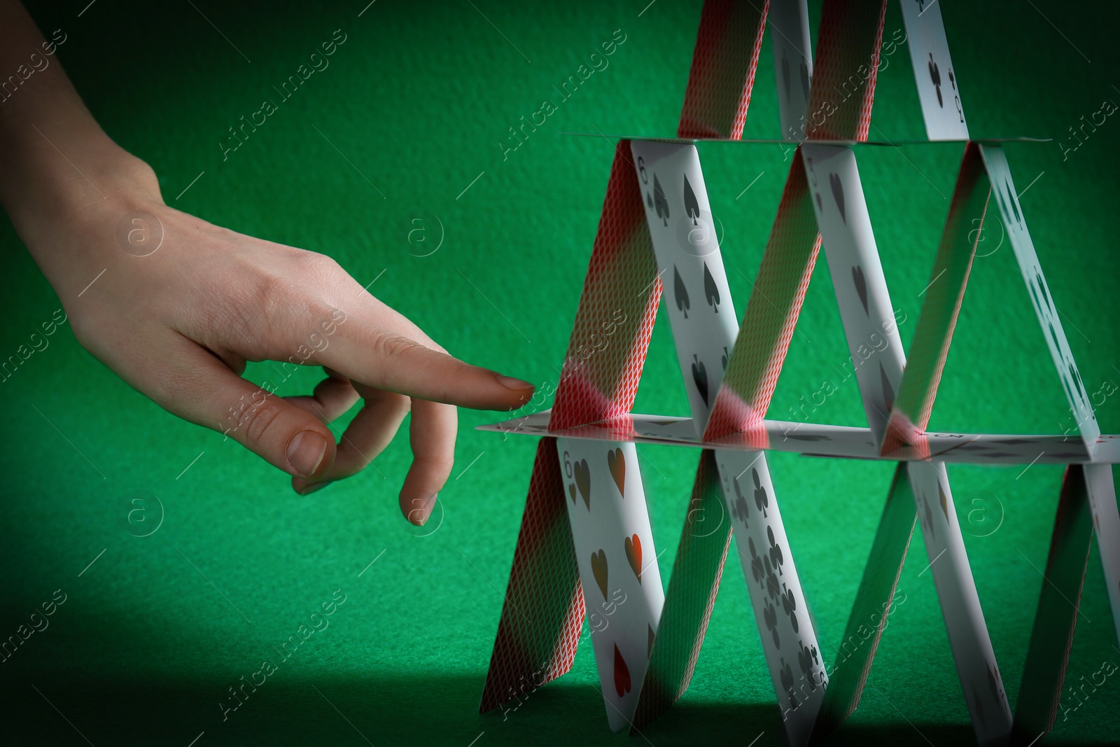 Photo of Woman destroying house of playing cards on green background, closeup