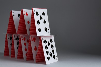 Photo of House of playing cards on grey background, closeup. Space for text