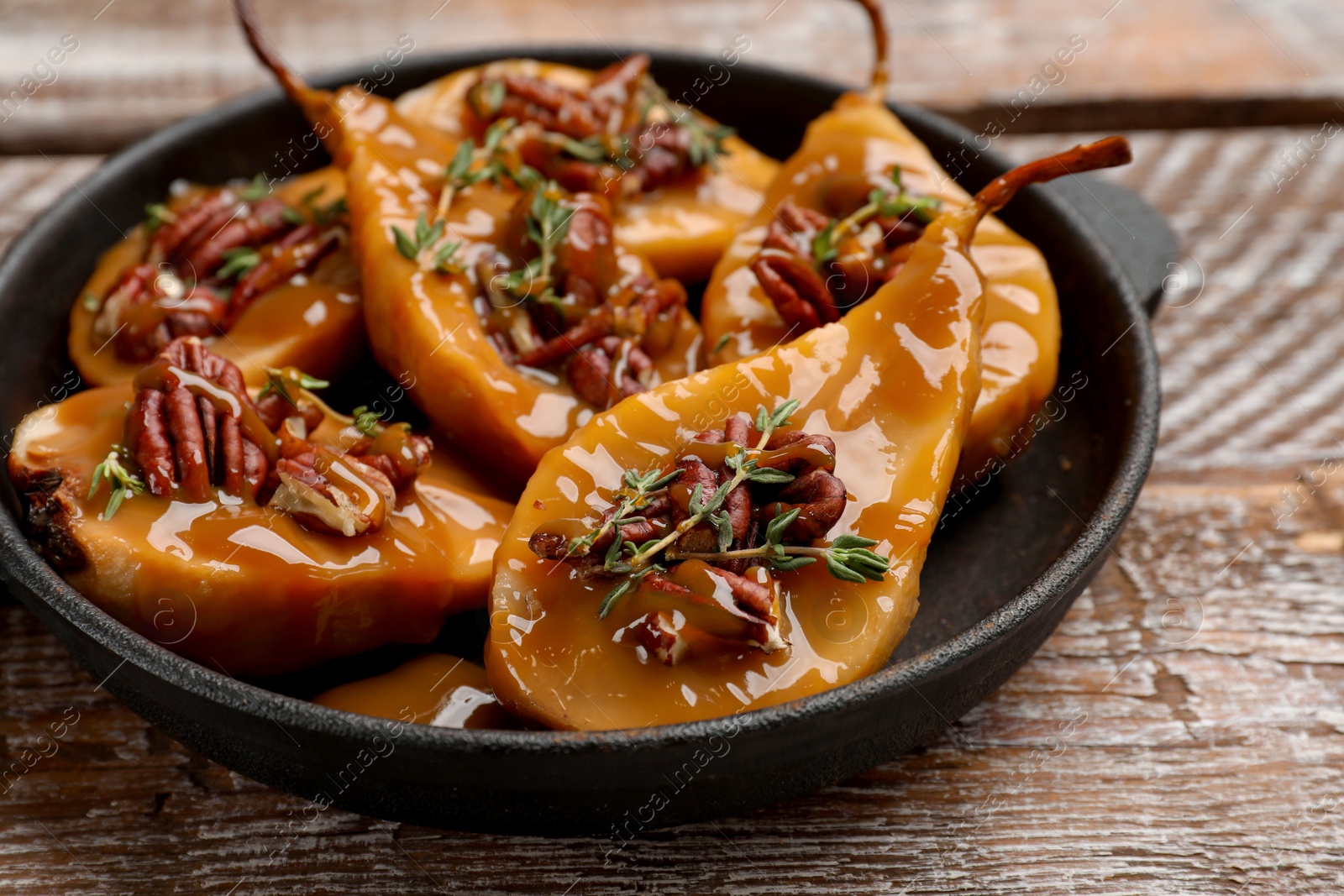 Photo of Delicious pears with caramel sauce, pecan nuts and thyme on wooden table, closeup