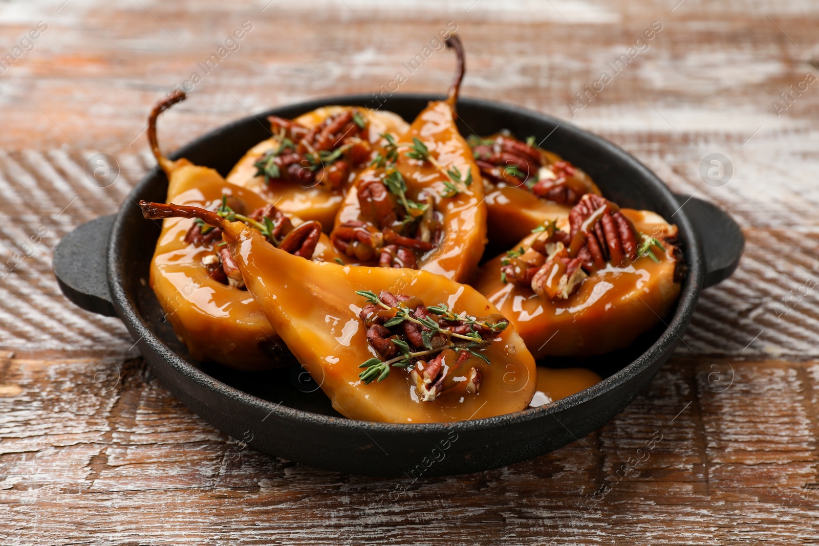 Photo of Delicious pears with caramel sauce, pecan nuts and thyme on wooden table, closeup