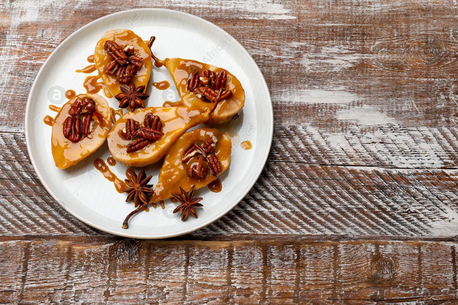 Photo of Delicious pears with caramel sauce, pecan nuts and anise stars on wooden table, top view. Space for text