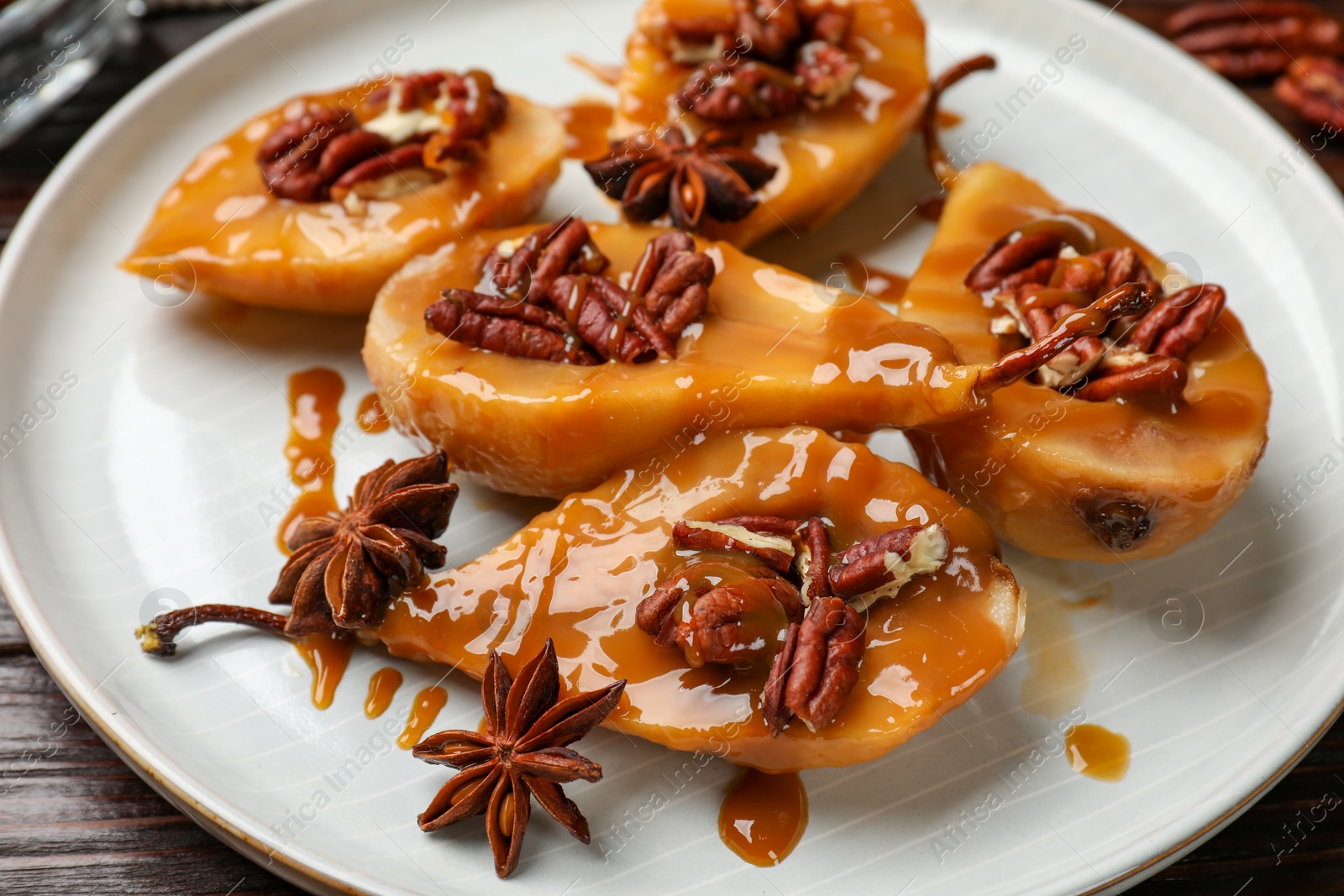 Photo of Delicious pears with caramel sauce, pecan nuts and anise stars on table, closeup