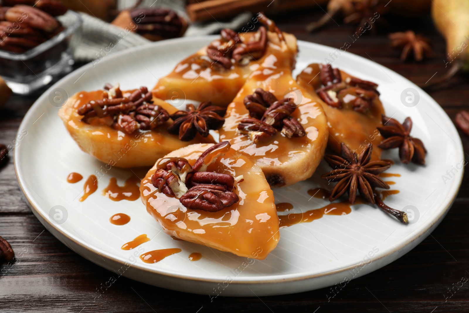 Photo of Delicious pears with caramel sauce, pecan nuts and anise stars on wooden table, closeup