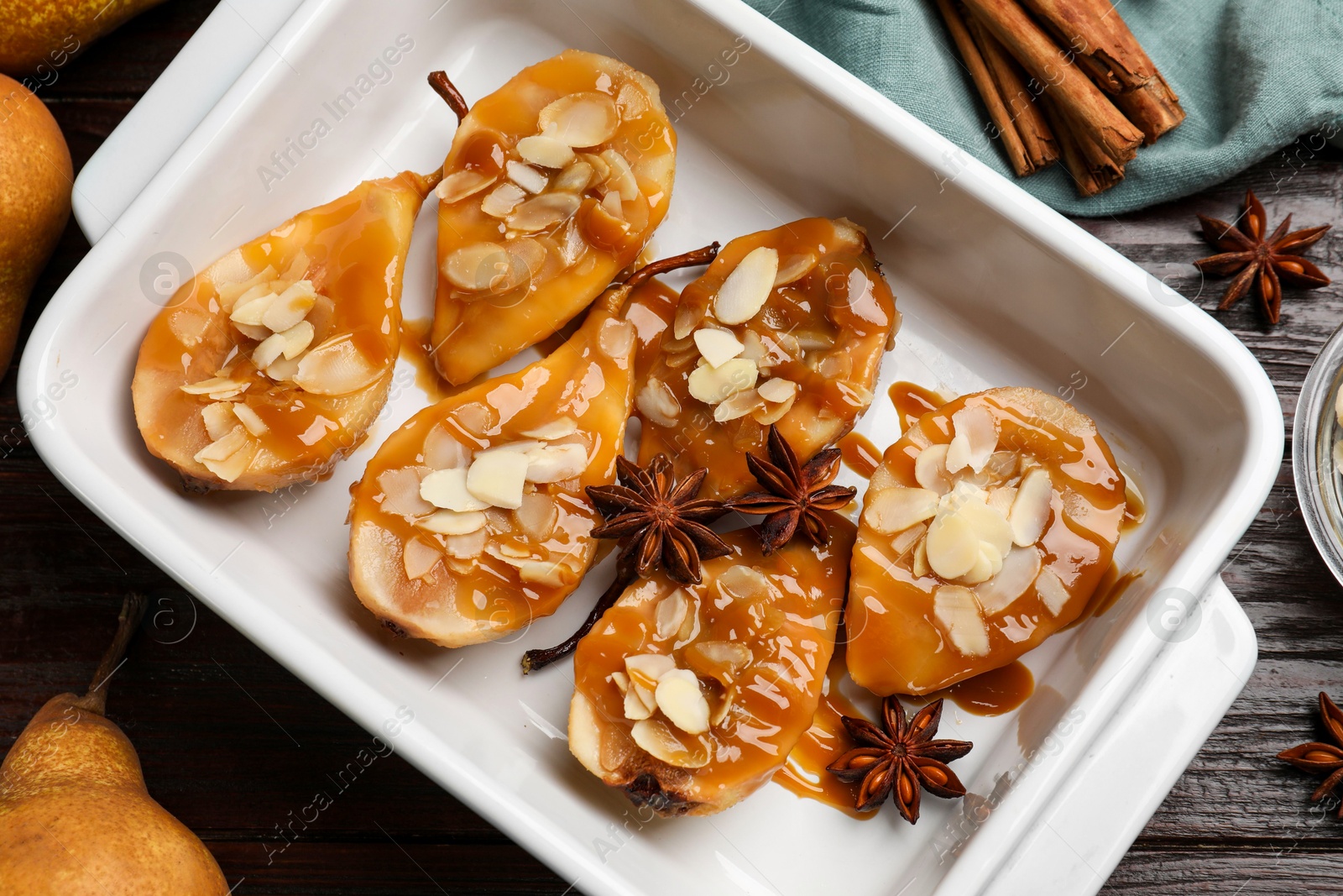 Photo of Delicious pears with caramel sauce, almond flakes and spices on wooden table, top view