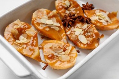 Photo of Delicious pears with caramel sauce, almond flakes and anise stars in baking dish on white marble table, closeup