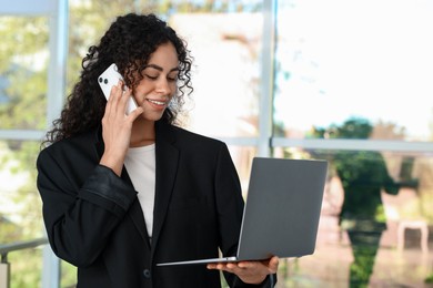 Photo of Portrait of young woman with laptop and phone wearing stylish suit indoors