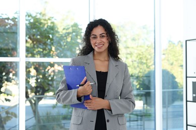 Photo of Portrait of young woman with clipboard wearing stylish suit indoors