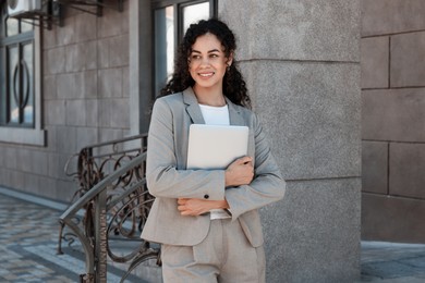 Portrait of young woman with laptop wearing stylish suit outdoors