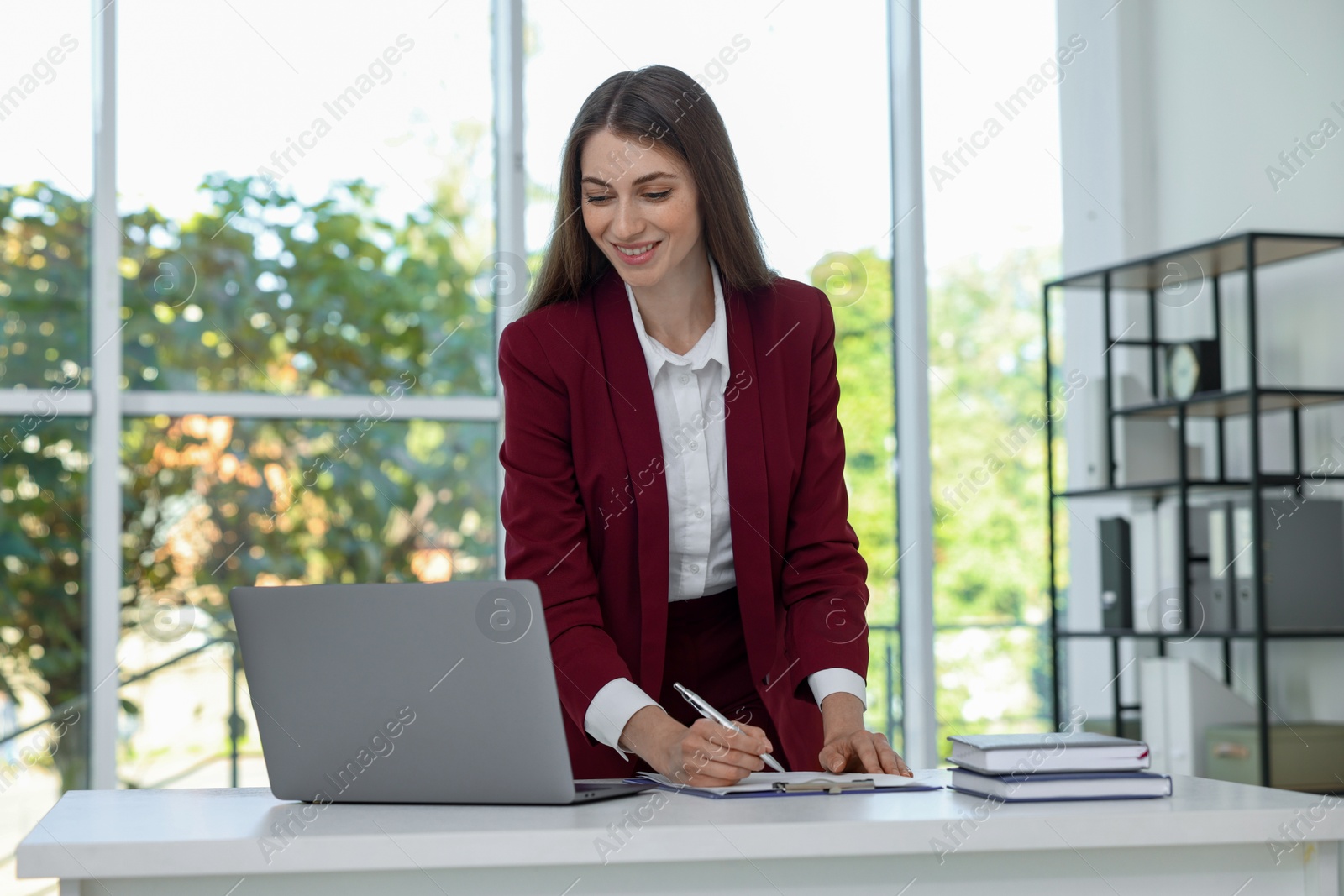 Photo of Portrait of young woman with laptop wearing stylish suit at white table indoors