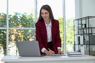 Portrait of young woman with laptop wearing stylish suit at white table indoors