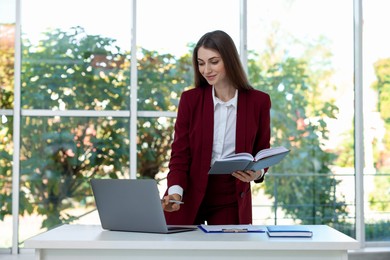 Photo of Portrait of young woman with laptop wearing stylish suit at white table indoors