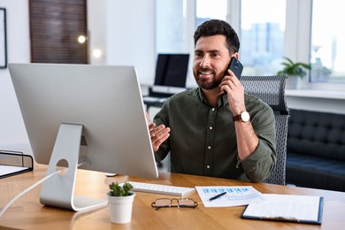 Photo of Man talking on smartphone while working at table in office