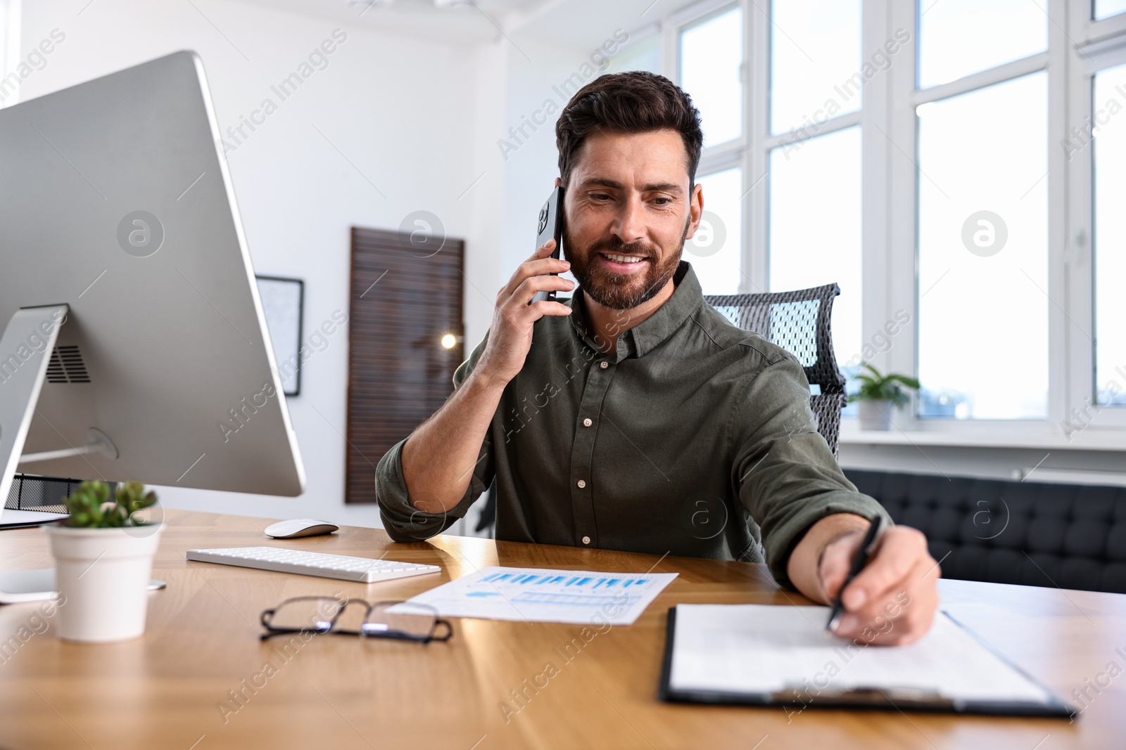 Photo of Man talking on smartphone while working at table in office