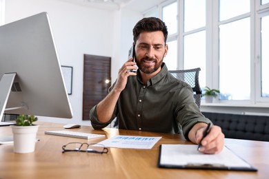 Photo of Man talking on smartphone while working at table in office