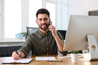 Photo of Man talking on smartphone while working at table in office