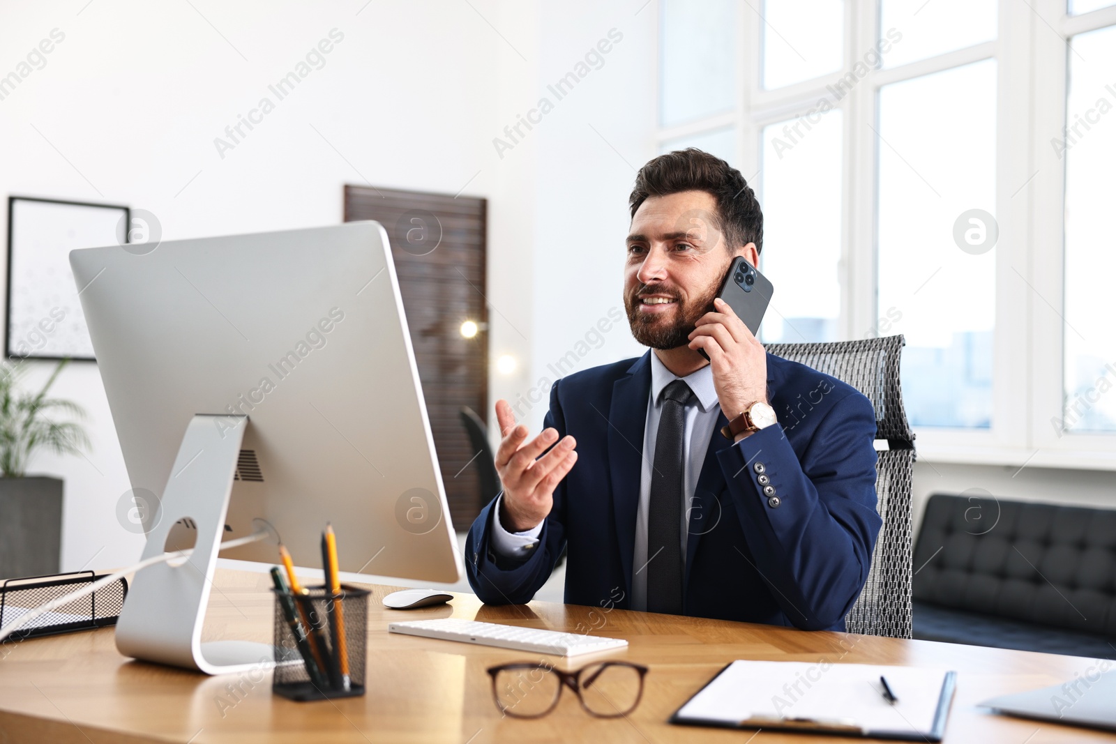 Photo of Man talking on smartphone while working at table in office