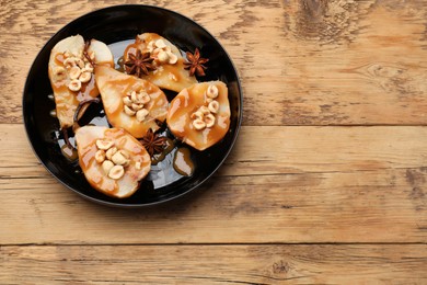 Photo of Delicious pears with caramel sauce, nuts and anise stars on wooden table, top view. Space for text