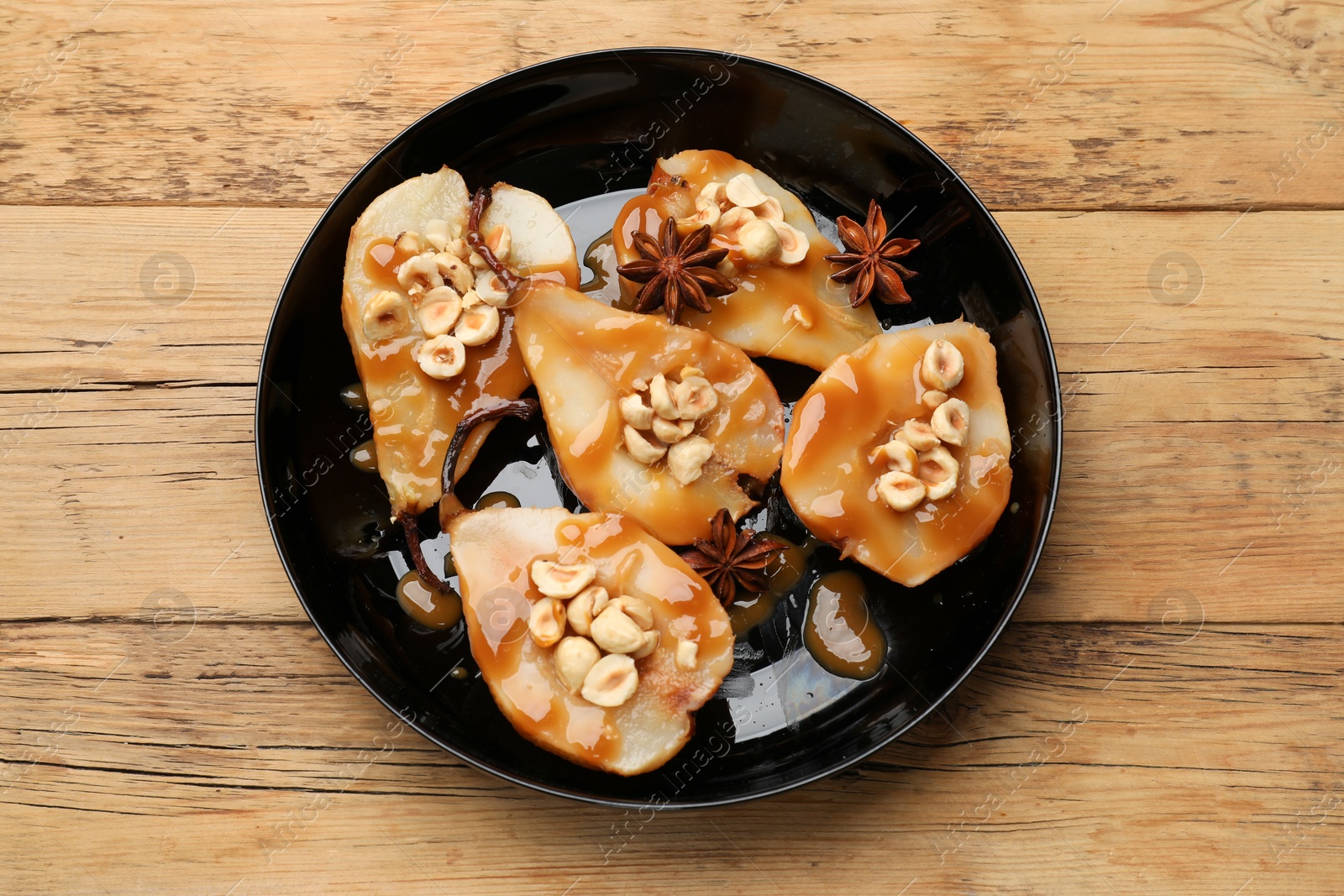 Photo of Delicious pears with caramel sauce, nuts and anise stars on wooden table, top view