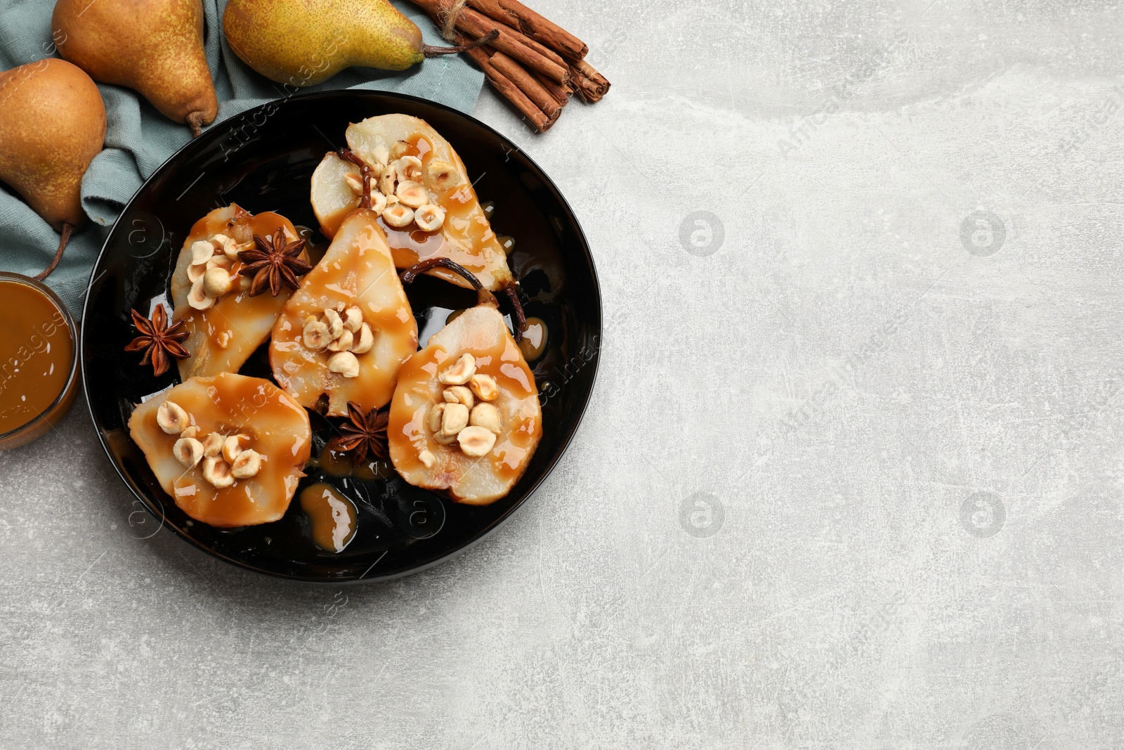 Photo of Delicious pears with caramel sauce, nuts and spices on grey table, top view. Space for text