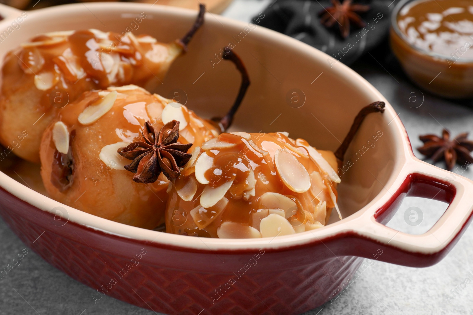 Photo of Delicious pears with caramel sauce and almond flakes in baking dish on grey table, closeup