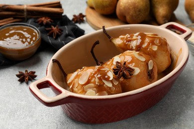 Photo of Delicious pears with caramel sauce, almond flakes and spices on grey table, closeup