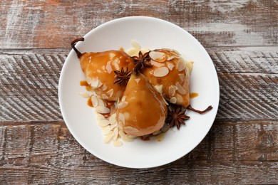 Photo of Delicious pears with caramel sauce, almond flakes and anise stars on wooden table, top view