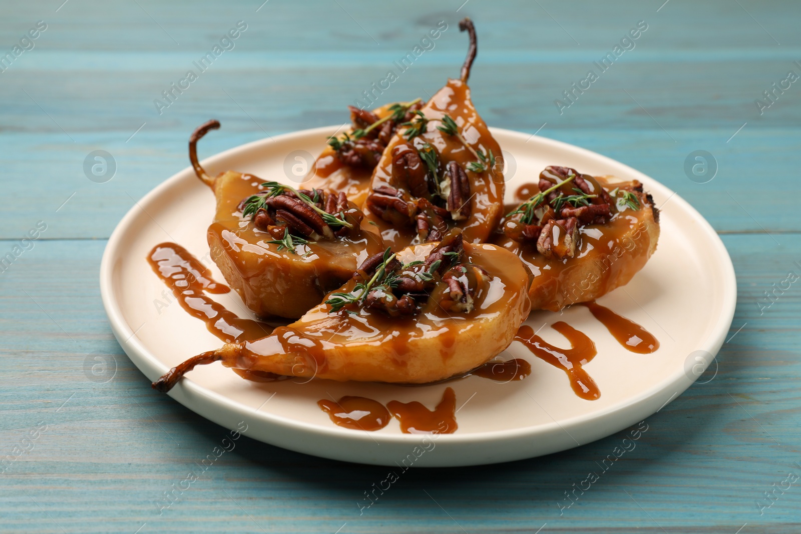 Photo of Delicious pears with caramel sauce, pecan nuts and thyme on light blue wooden table, closeup