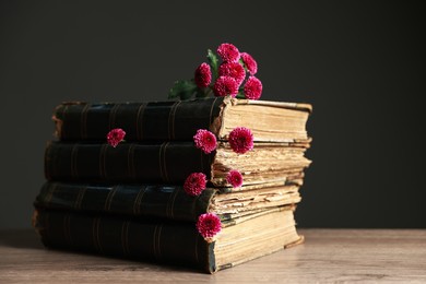 Photo of Stack of books and beautiful flowers on table against black background, closeup