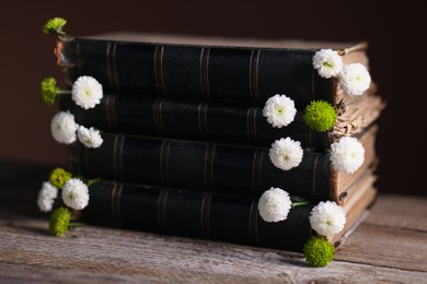 Photo of Stack of books with beautiful flowers on wooden table, closeup