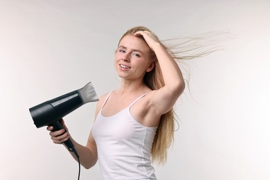 Photo of Beautiful young woman drying her hair with hairdryer on light grey background