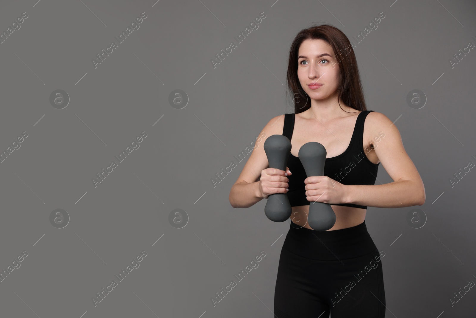 Photo of Woman in sportswear exercising with dumbbells on grey background, space for text