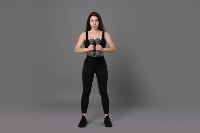 Photo of Woman in sportswear exercising with dumbbells on grey background