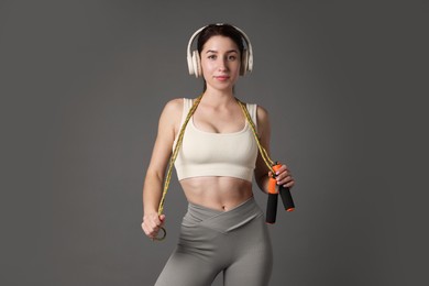 Photo of Woman in sportswear with headphones and skipping rope on grey background