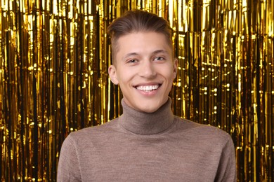 Photo of Happy young man against golden foil curtain