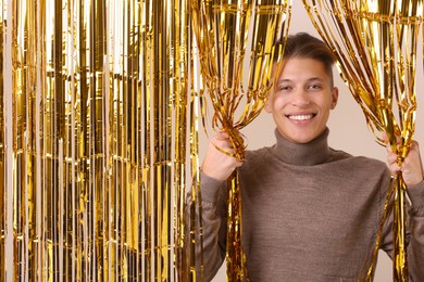 Photo of Happy young man near golden foil curtain against beige background