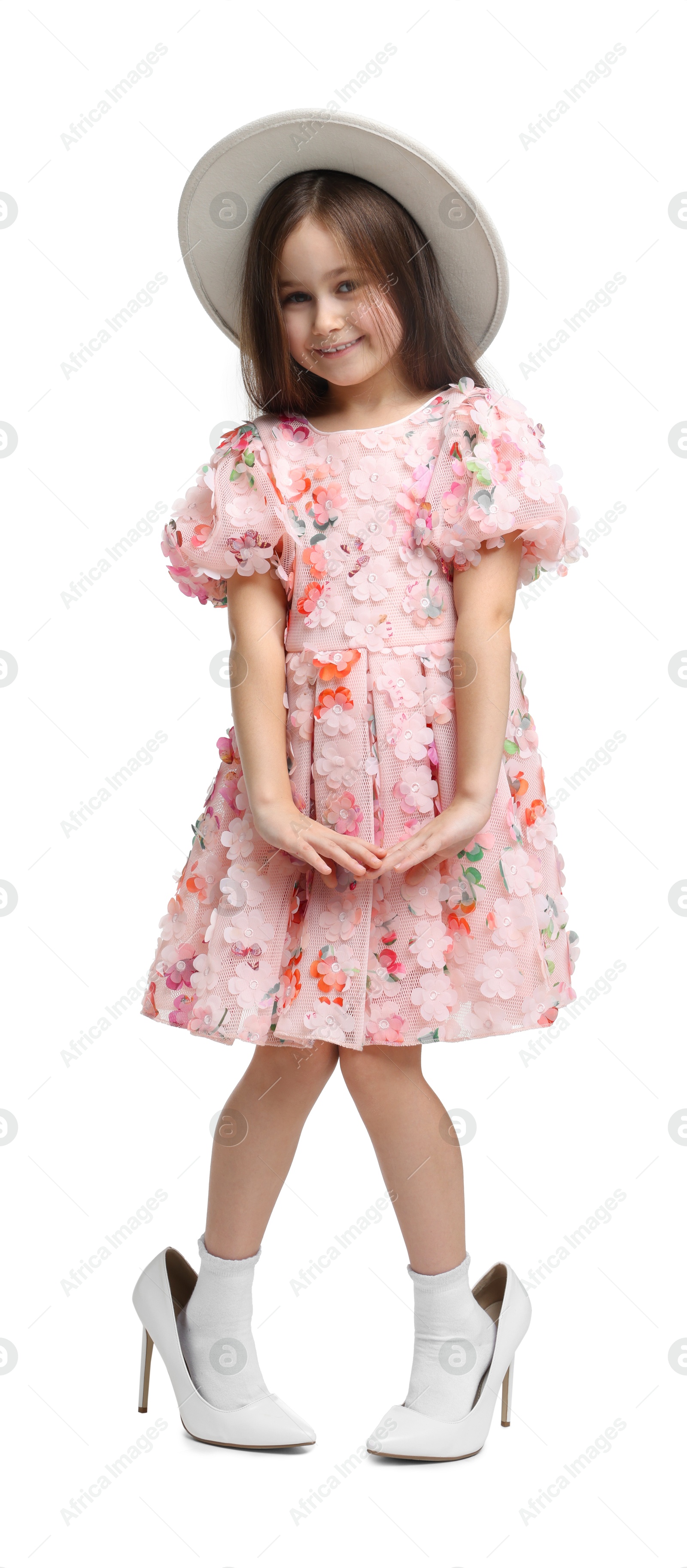 Photo of Stylish little girl wearing oversized high heeled shoes on white background