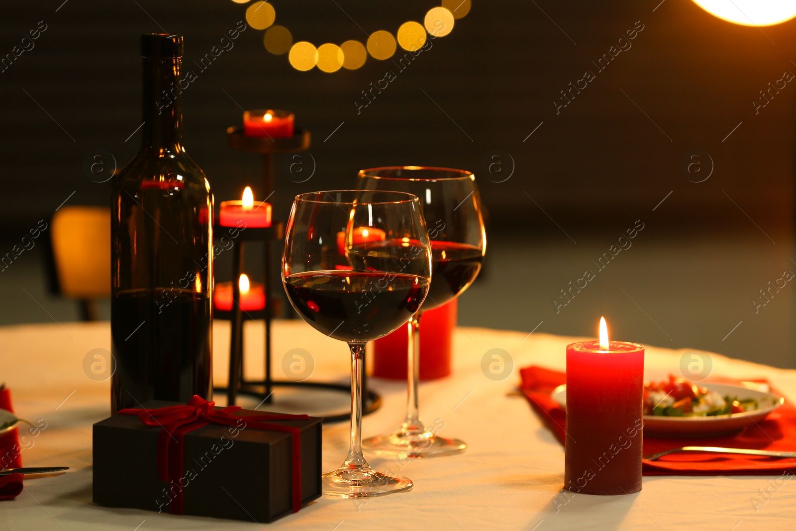 Photo of Red wine, burning candles and gift box on table. Romantic dinner