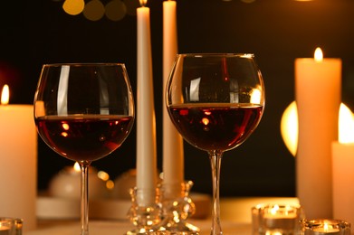 Photo of Glasses of red wine and burning candles against blurred lights, closeup. Romantic dinner