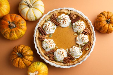 Photo of Delicious homemade pumpkin pie in baking dish and fresh pumpkins on orange table, flat lay