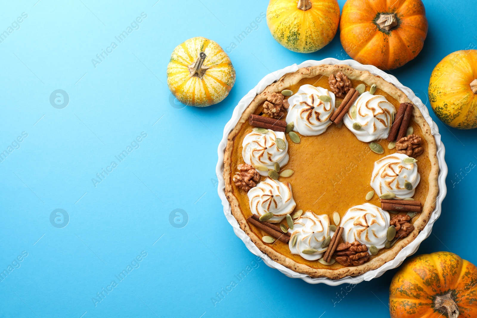 Photo of Delicious homemade pumpkin pie in baking dish and fresh pumpkins on light blue table, flat lay. Space for text