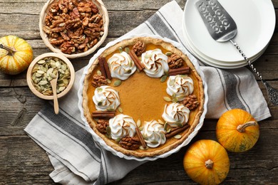 Photo of Tasty homemade pumpkin pie in baking dish and ingredients on wooden table, flat lay