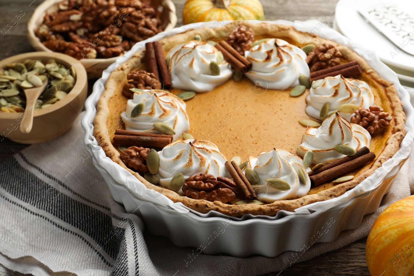 Photo of Tasty homemade pumpkin pie in baking dish and ingredients on wooden table, closeup