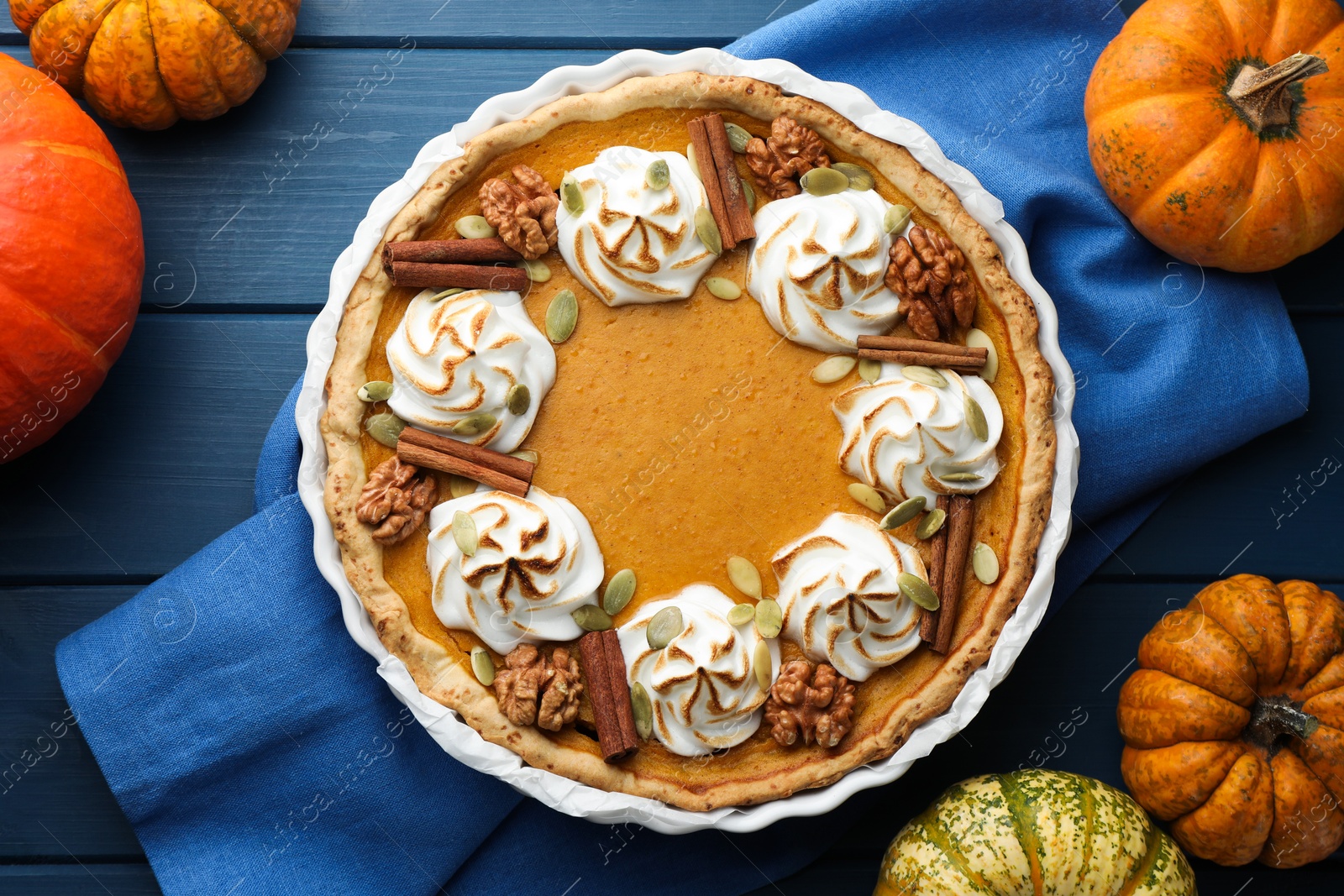 Photo of Delicious homemade pumpkin pie in baking dish and fresh pumpkins on blue wooden table, flat lay