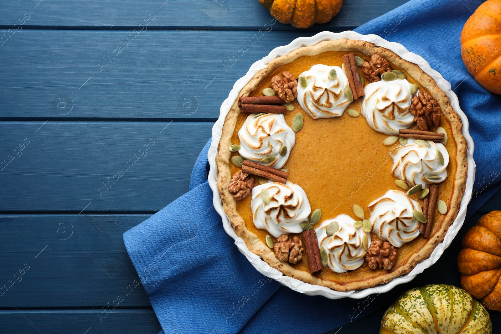 Photo of Delicious homemade pumpkin pie in baking dish and fresh pumpkins on blue wooden table, flat lay. Space for text