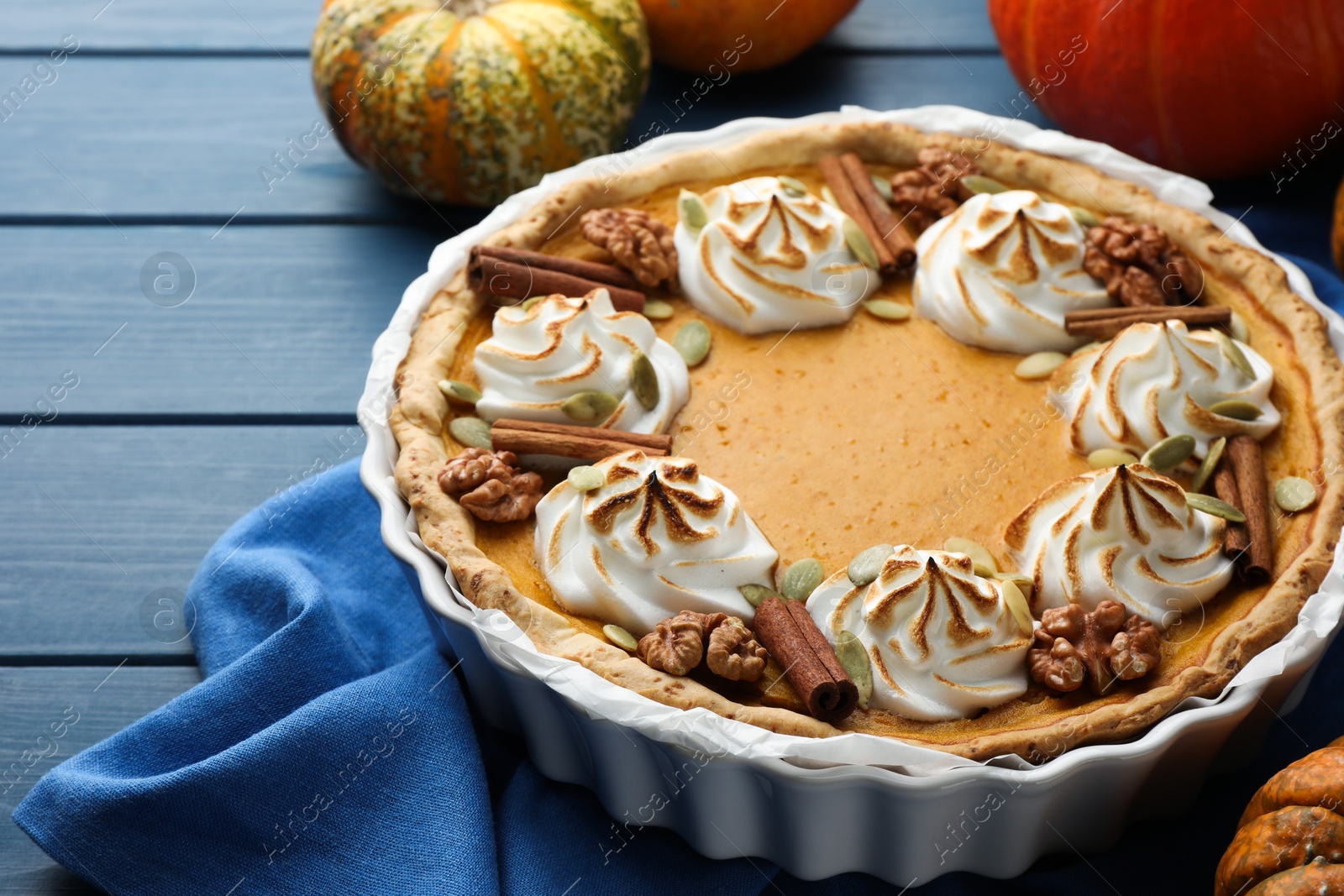 Photo of Delicious homemade pumpkin pie in baking dish and fresh pumpkins on blue wooden table, closeup