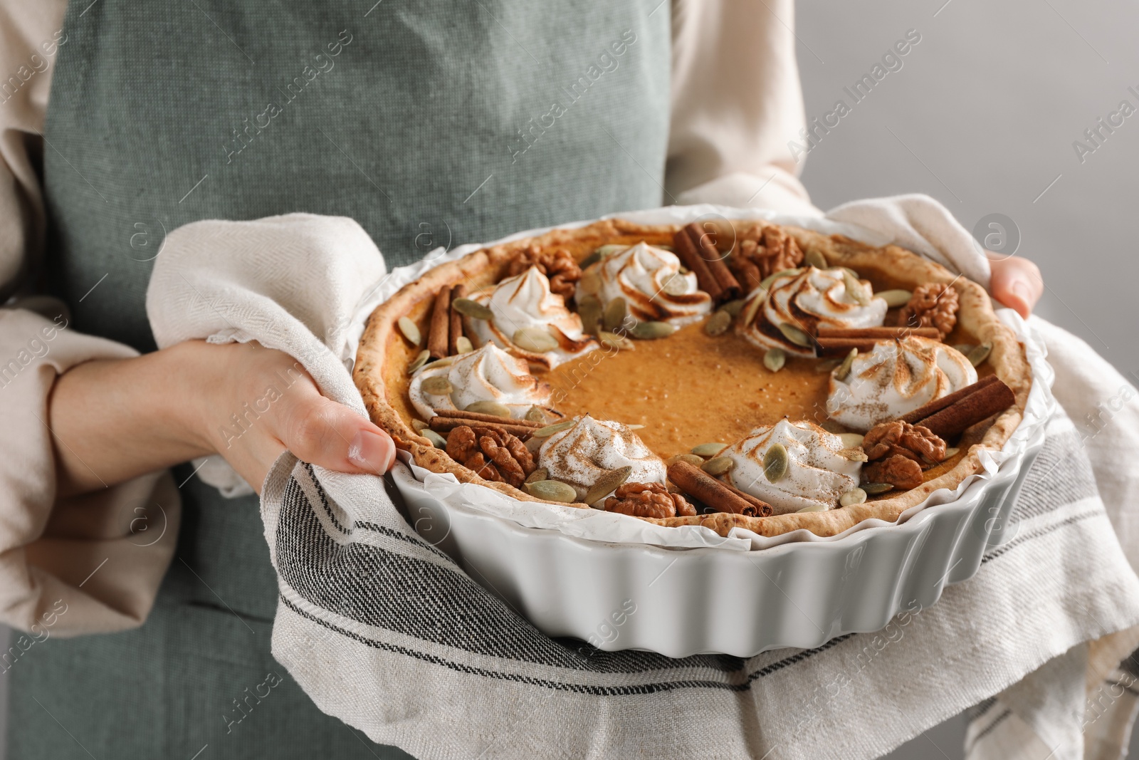 Photo of Woman holding homemade pumpkin pie with whipped cream, seeds and cinnamon on grey background, closeup