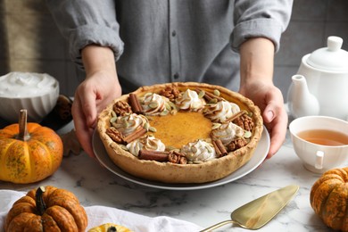 Photo of Woman with homemade pumpkin pie with whipped cream, seeds and cinnamon at white marble table, closeup